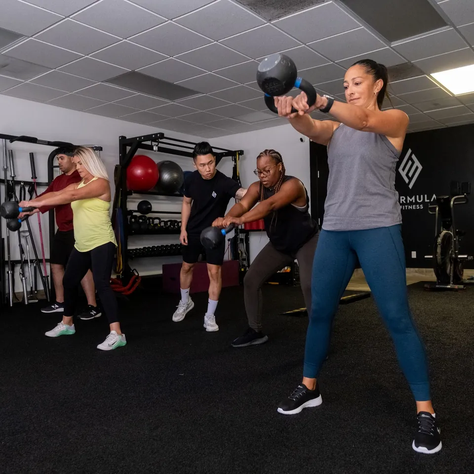 A Formula Fitness coach guiding a small group through a two-handed kettlebell swing
